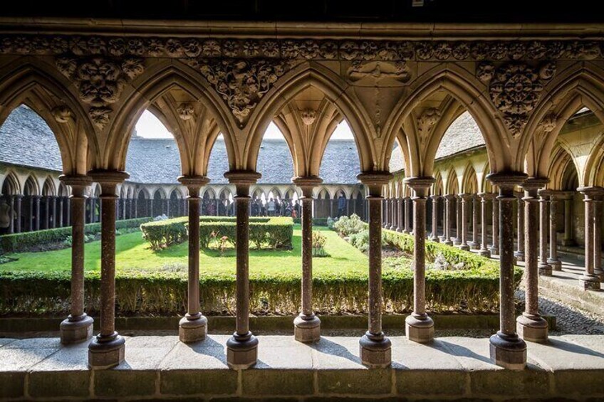 A cloister with arched walkways and columns, overlooking a well-manicured garden and a body of water. 3