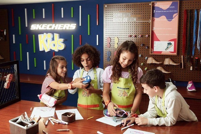 Niños participan en actividades de diseño de zapatos en un aula con un cartel de 'Skechers Kids'. 3