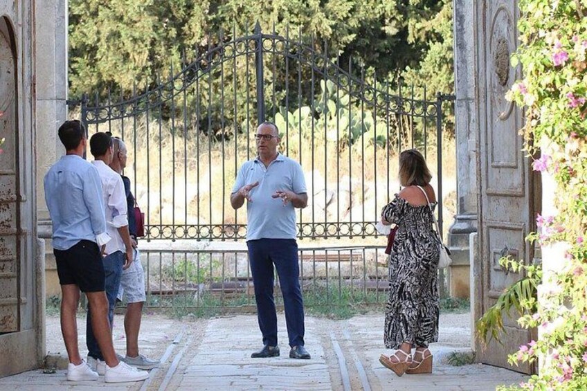A group of people standing in a garden with a wrought iron gate and stone architecture. 2