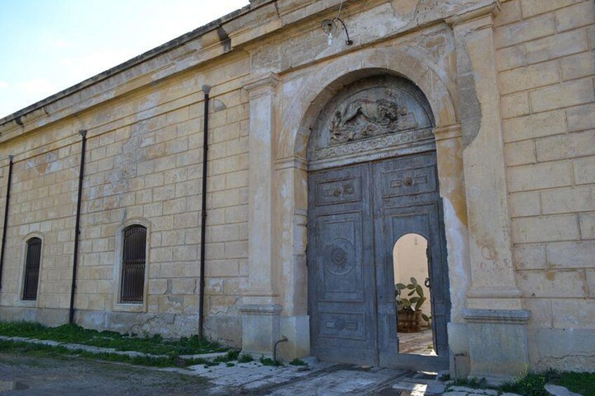 A historic building with a large arched entrance, a decorative relief above the door, and a small window to the left. 5