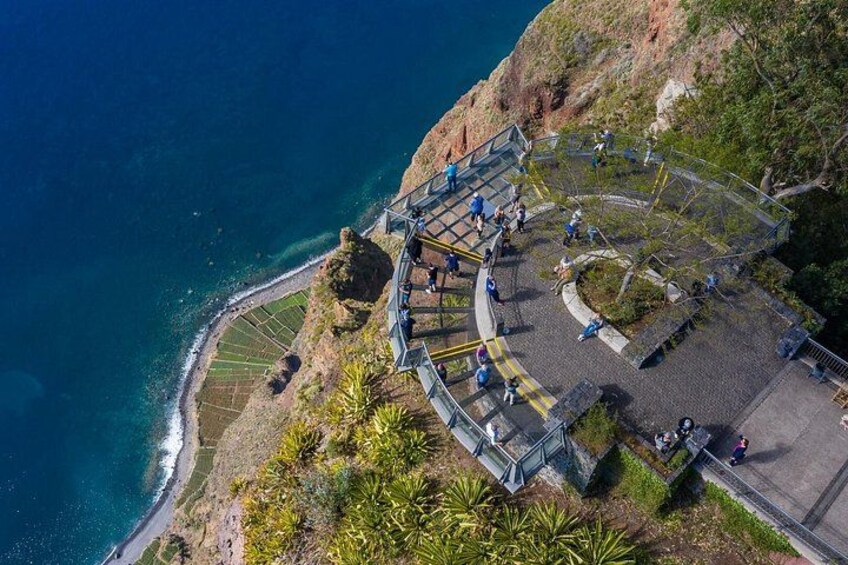 A coastal viewpoint with a glass bridge, a paved walkway, and a rocky cliff. 2