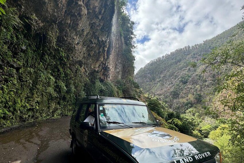 A Land Rover on a narrow mountain road surrounded by lush greenery and steep cliffs. 3
