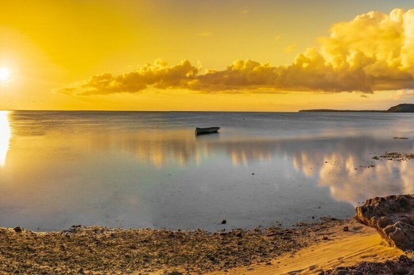 Een rustige zee bij zonsondergang met een boot, een zandstrand en land in de verte. 3