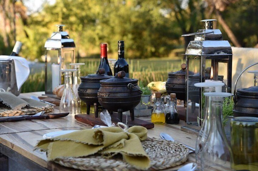 A rustic outdoor setting with cooking equipment, bottles, and jars on a wooden table. 5