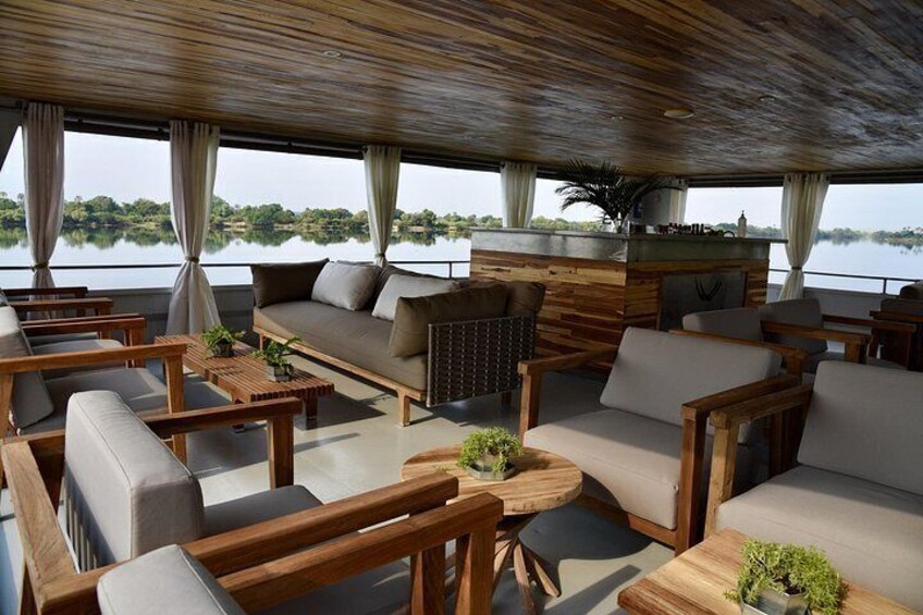 A spacious outdoor seating area with wooden furniture and cushions, overlooking a calm body of water. 4