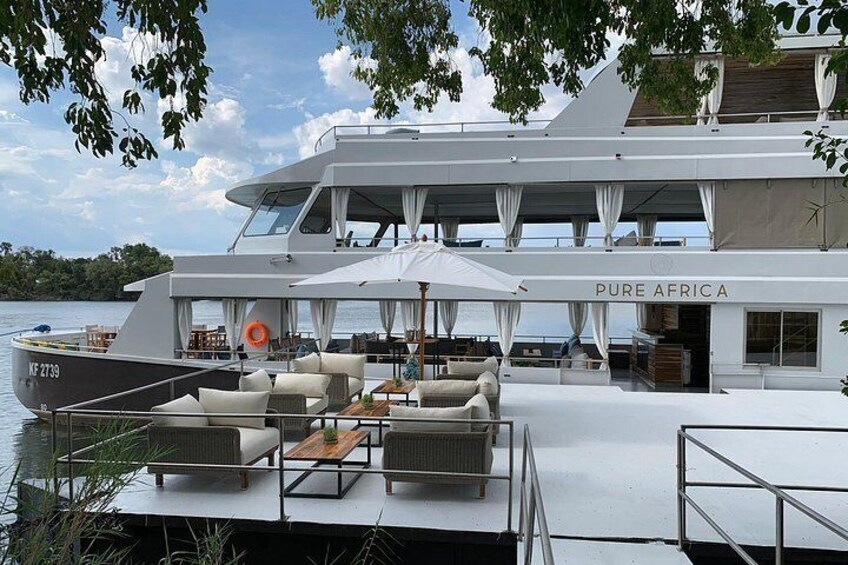 A large yacht named 'PURE AFRICA' docked at a marina with outdoor seating and a covered area. 3