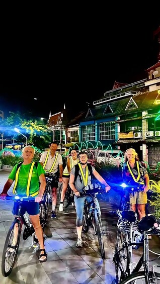 A group of people on bicycles with safety vests, riding on a paved path at night. 4