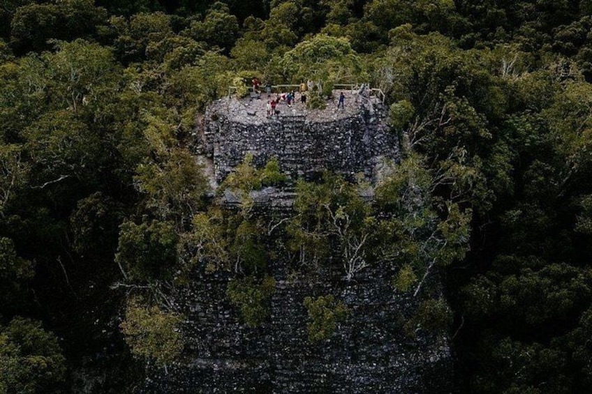 A rocky outcrop with people standing on top, surrounded by dense forest. 3