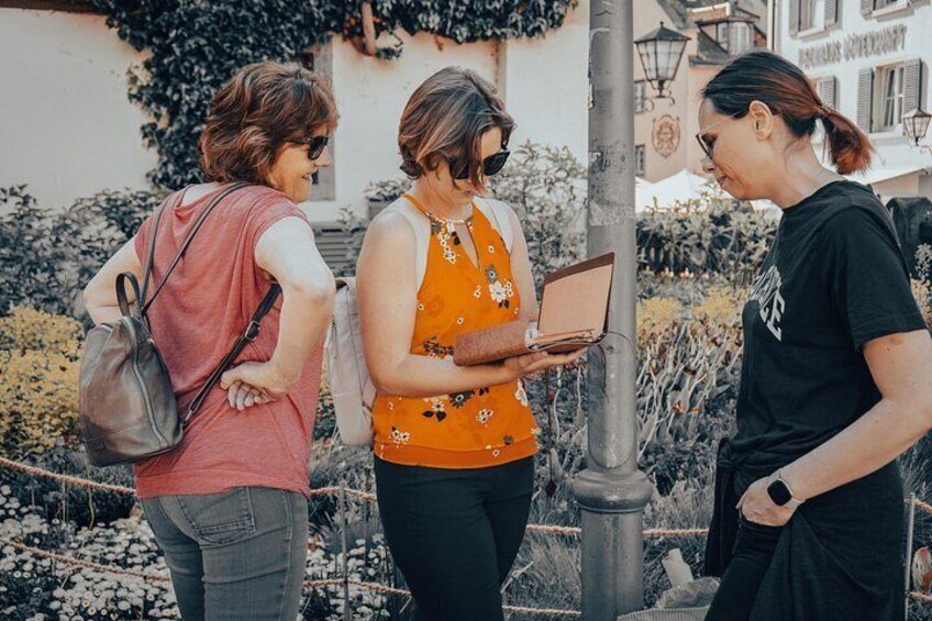 Tres personas al aire libre, una sosteniendo una computadora portátil, con un edificio y vegetación de fondo. 1