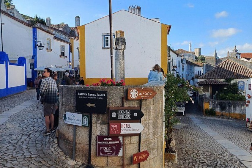 Una calle adoquinada con un poste indicador que muestra direcciones a diversas atracciones y alojamientos locales. 3