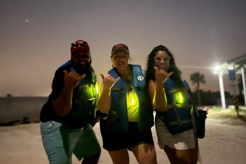 Drei Personen in Schwimmwesten stehen an einem Strand bei Dämmerung. 5