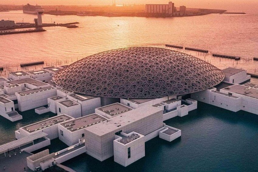 Un edificio grande y circular con techo decorado, rodeado de construcciones más pequeñas y una orilla de agua. 2