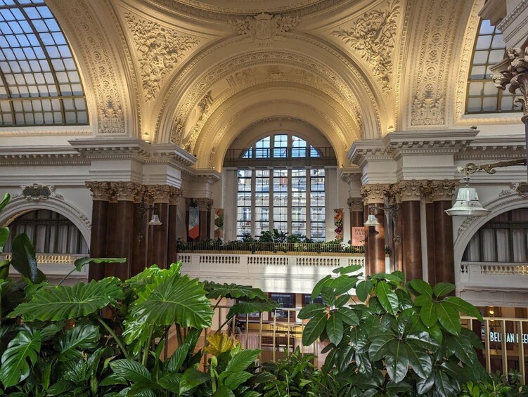 Een weelderig interieur met een hoog, gewelfd plafond, grote ramen en overvloedige begroeiing. 1