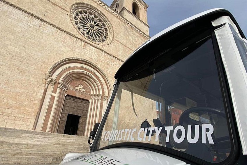 A tour bus in front of a historic building with a large circular window and a bell tower. 2