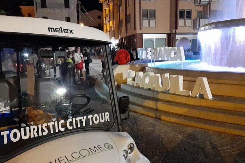 Un autobus touristique portant l’inscription « VISITE GUIDÉE DE LA VILLE » était stationné près d’une fontaine, à côté de panneaux indiquant « MEI BIANCA » et « TEQUILA ». 3