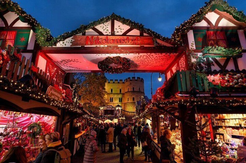 A festive market with a prominent archway labeled 'Nikolausmarkt,' surrounded by stalls and illuminated by string lights. 4