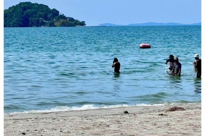 Una playa con gente vadeando en el agua, una pequeña isla a lo lejos, y cielo despejado. 4