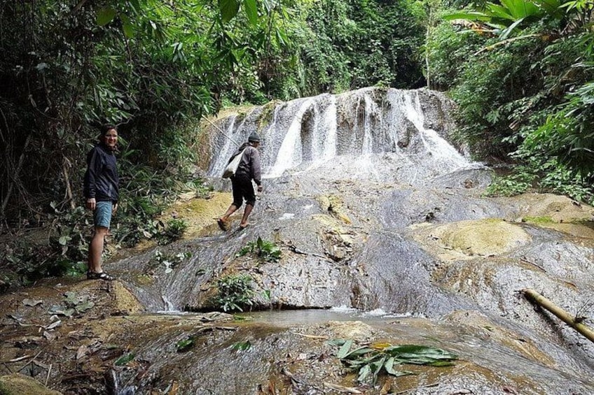 A waterfall in a forested area with two people walking nearby. 5