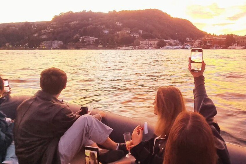 Personas en un bote, fotografiando un atardecer sobre un lago con edificios al fondo. 3