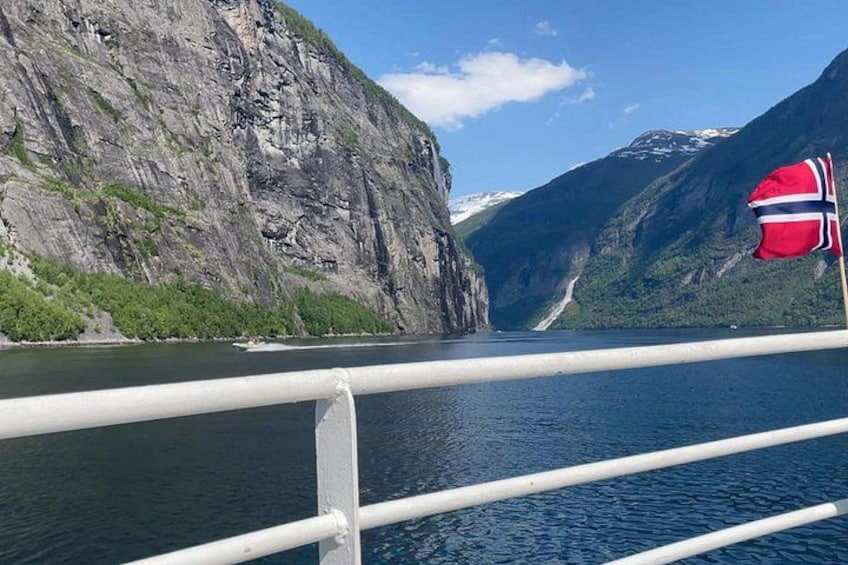 A fjord with steep cliffs, a Norwegian flag, and a clear blue sky. 3