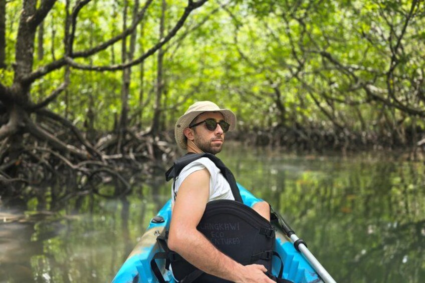 En person i en kajak på stille vand omgivet af tæt mangrove. 4