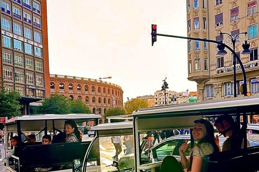 A green trolley with passengers, a red traffic light, and a large building with arched windows in the background. 1