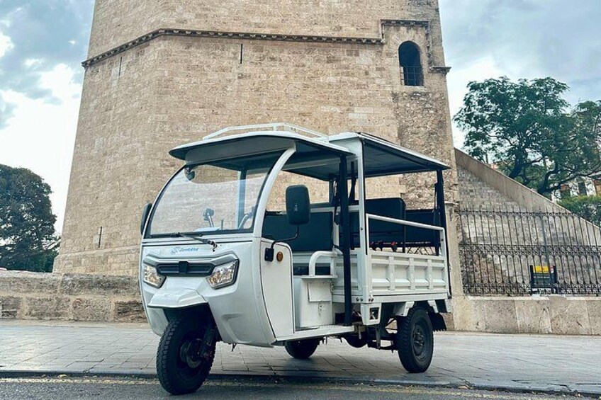 Un véhicule blanc à trois roues est garé devant un grand bâtiment en pierre doté d’un clocher. 3