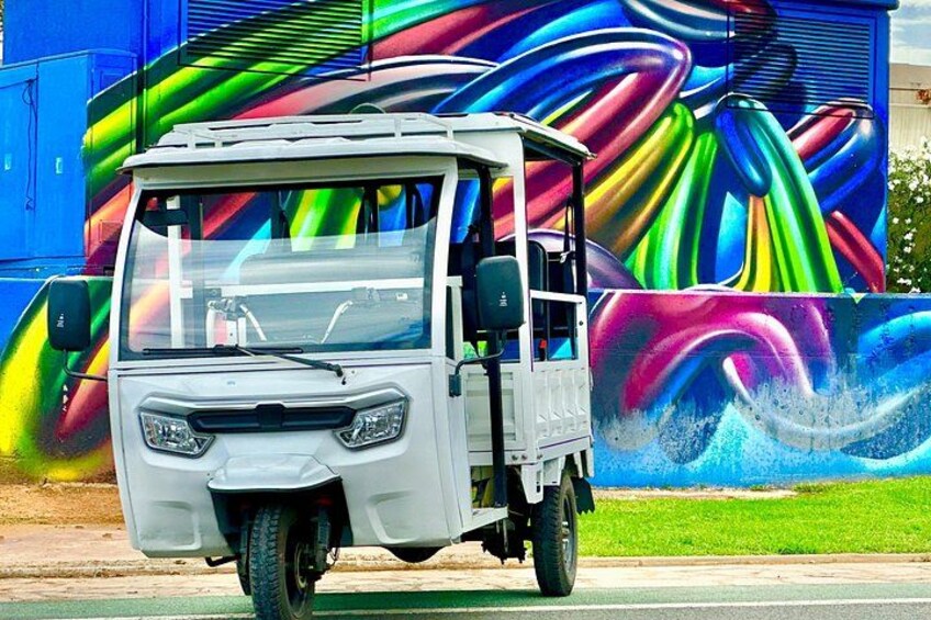 Un véhicule blanc à trois roues est garé devant une fresque murale aux couleurs vives. 2