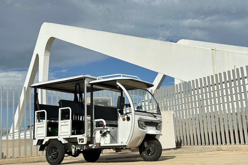 A white three-wheeled vehicle parked in front of a white bridge structure. 5