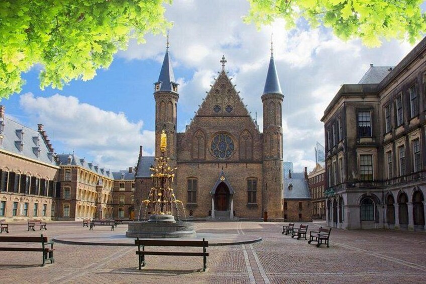 En historisk kirke med to tårne, en springvand og bænke på en plads. 4