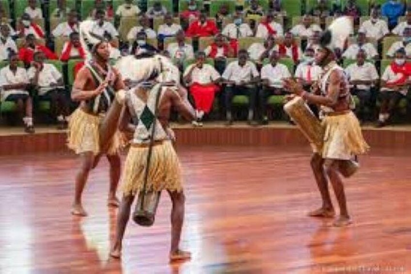 A group of dancers in traditional attire performing on a wooden floor with an audience in the background. 4