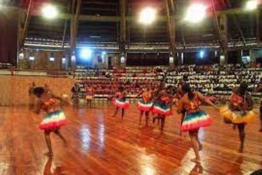 A dance performance in a large indoor venue with a wooden floor and rows of seating. 5