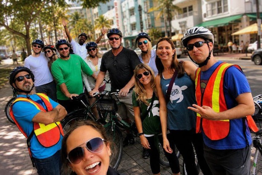 A group of people with bicycles, some wearing helmets and reflective vests, standing on a sidewalk. 5