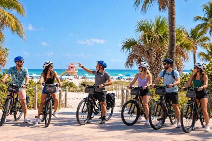 A group of people on bicycles along a coastal path with palm trees and a beach in the background. 2