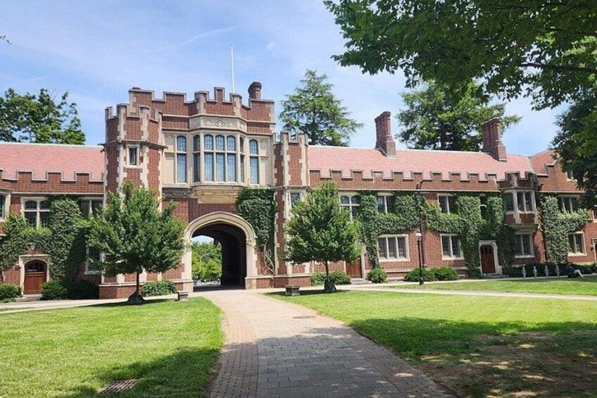 Un grande edificio in mattoni con un arco centrale, circondato da prati curati e alberi. 3