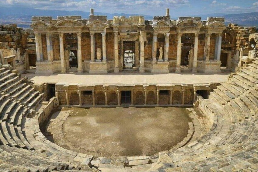 Un antiguo anfiteatro con asientos de piedra y un escenario central. 2