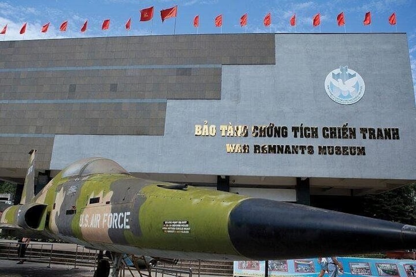 Una aeronave militar con la inscripción 'U.S. AIR FORCE' y 'MUSEO DE LOS REMANENTES DE LA GUERRA', frente a un edificio con banderas vietnamitas y un logotipo. 5
