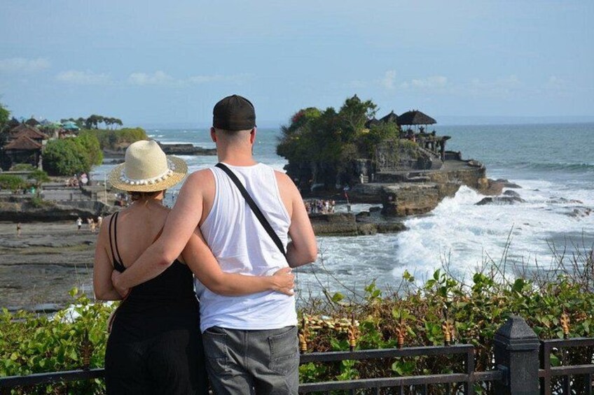 A couple standing by a rocky coastline with waves crashing below. 3