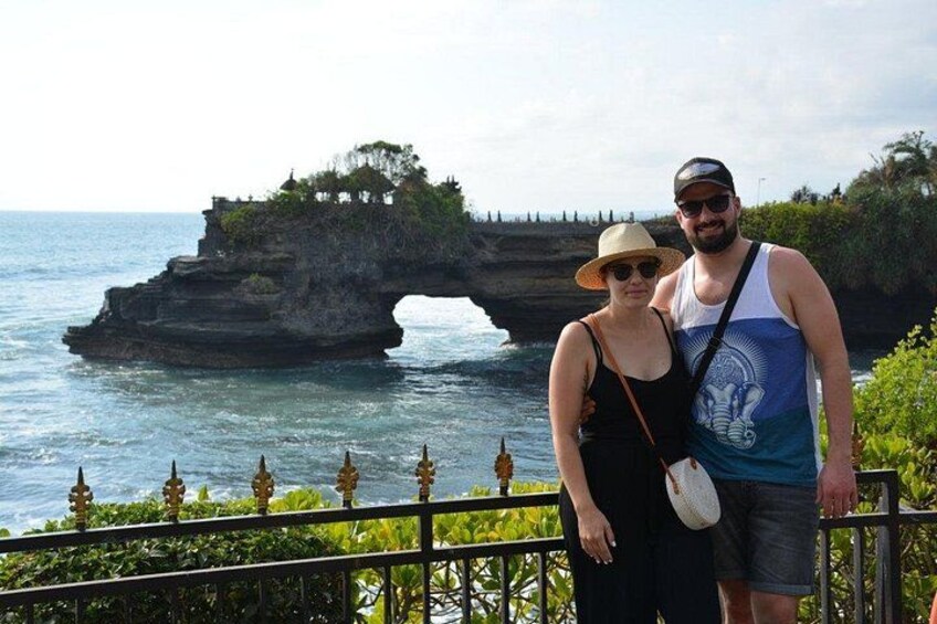 A couple standing by a coastal cliff with a natural rock formation. 2