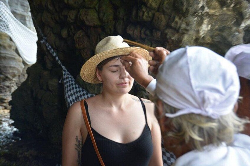 A person wearing a straw hat and a black tank top, standing outdoors with a stone wall in the background. 5