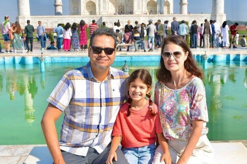 A family in front of the Taj Mahal with a pool and visitors in the background. 1
