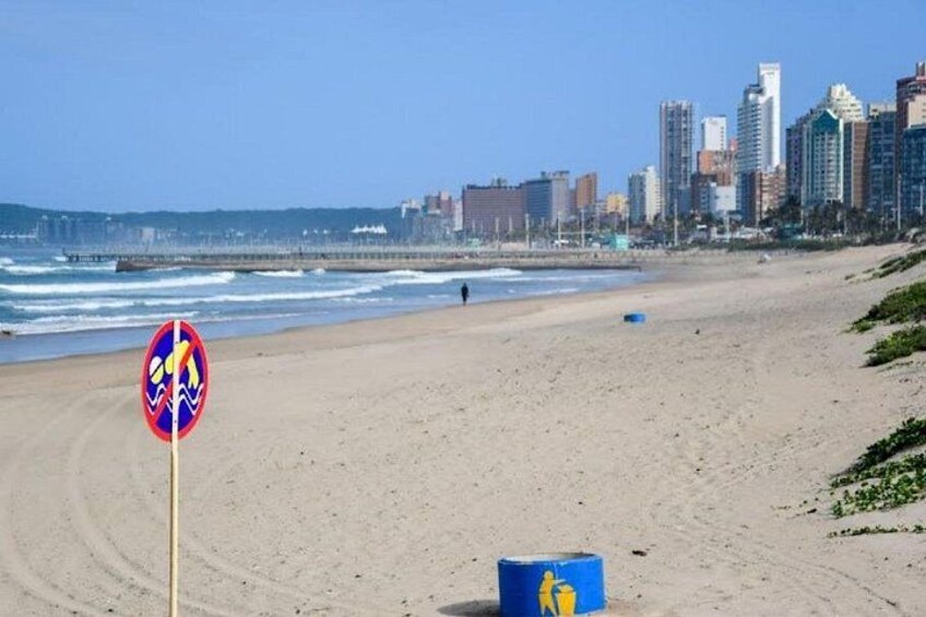 A beach with a no swimming sign, a blue barrel, and a city skyline in the background. 4