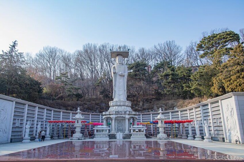 A large statue in a courtyard with a reflective pool, surrounded by white structures and trees in the background. 4
