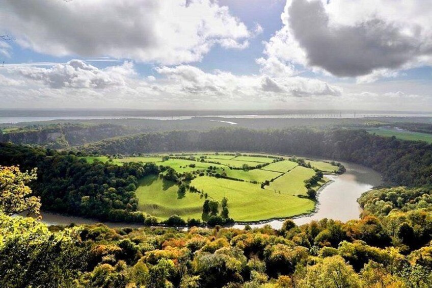 A river meandering through a green valley with fields, surrounded by hills and a cloudy sky. 3