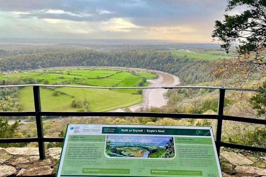 A scenic overlook with a river, green fields, and a signboard. 2