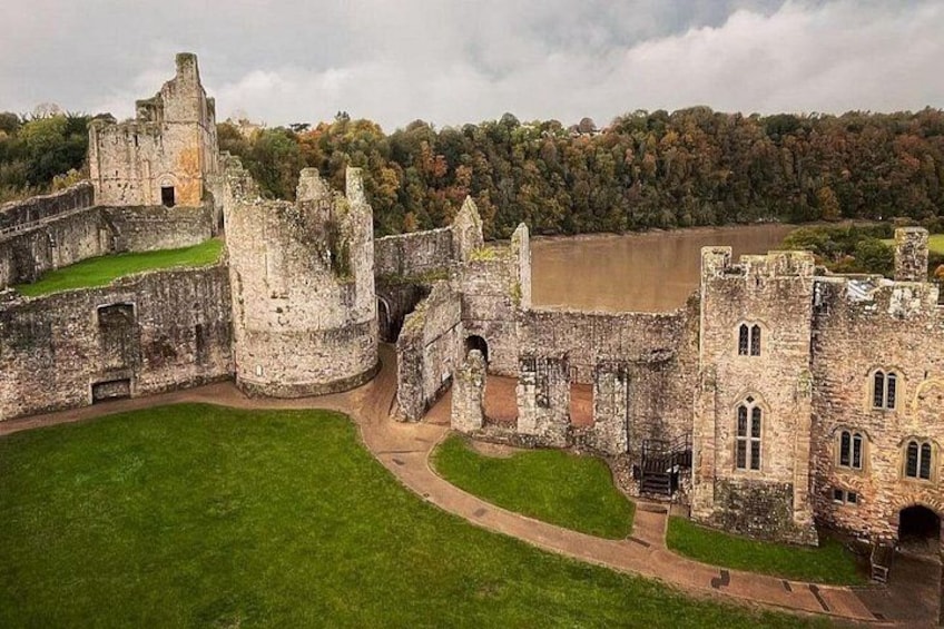 A historic castle with ruins, a grassy courtyard, and a forested background. 1