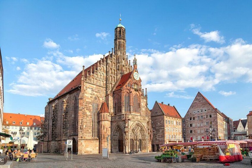 A historic church with a tall spire, a market area with stalls, and traditional buildings. 2
