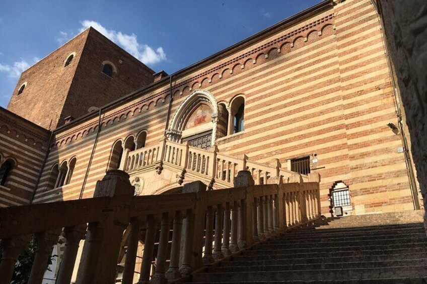 A historic building with a large arched entrance, a bell tower, and a staircase leading up to the entrance. 2
