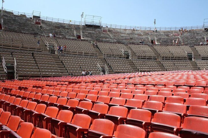 An empty stadium with red seats and a few people on the upper levels. 5