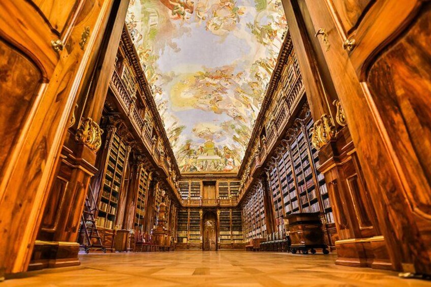 Ett storslaget bibliotek med hyllor i trä och ett detaljrikt, målat tak. 2